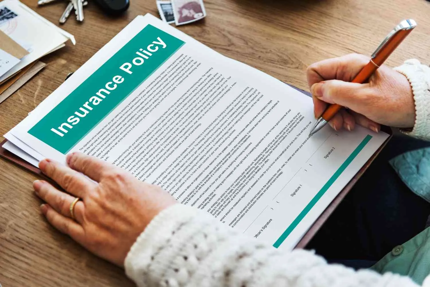A hand signing an insurance policy document at a table
